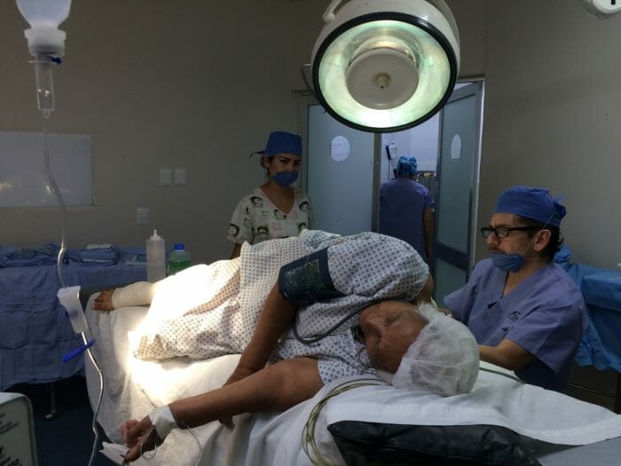 Elderly woman lies on a hospital bed and gets checked by a doctor.
